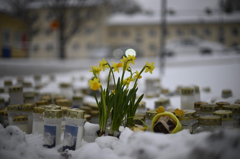 Candles and flowers are placed in the snow in front of the Viertola School to pay tribute to victims in Vantaa, in the north of the Finnish capital Helsinki, on April 3, 2024, one day after a 12-year-old opened fire inside the school, killing a classmate and seriously injuring two other children. Photo by Olivier MORIN / AFP