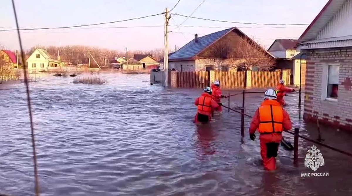 This photo taken from a video released by the Russian Emergency Situations Ministry on April 6, 2024 shows rescuers walking across a flooded street on their way to evacuate residents during a flood in the town of Orsk, Orenburg region, southeast of the southern tip of the Ural Mountains. (Photo by Handout / Russian Emergencies Ministry / AFP