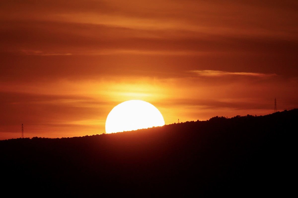 This photograph taken in Athens, Greece on April 5, 2024 shows the sun set behind a hill. (Photo by David GANNON / AFP)
