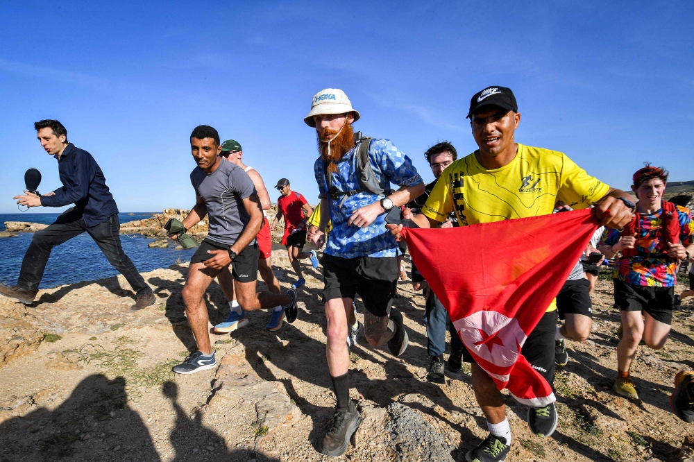 British runner Russ Cook (C) is joined by supporters on the final leg of his 16,000 kilometre challenge to run across the African continent from South Africa's Cape Agulhas to Tunisia's Cape Angela to raise money for charity, near Cape Angela, northeast of Tunis, on April 7, 2024. (Photo by FETHI BELAID / AFP)
