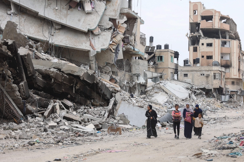 Palestinian women and children walk past the ruins of buildings destroyed by earlier Israeli bombardment in Gaza City on April 8, 2024. (Photo by AFP)
