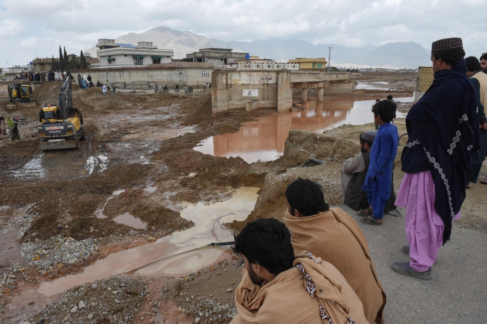 Onlookers gaze towards municipal workers using heavy machinery to level the ground after damage due to floodwaters following heavy rains on the outskirts of Quetta on April 15, 2024. (Photo by Banaras Khan / AFP)