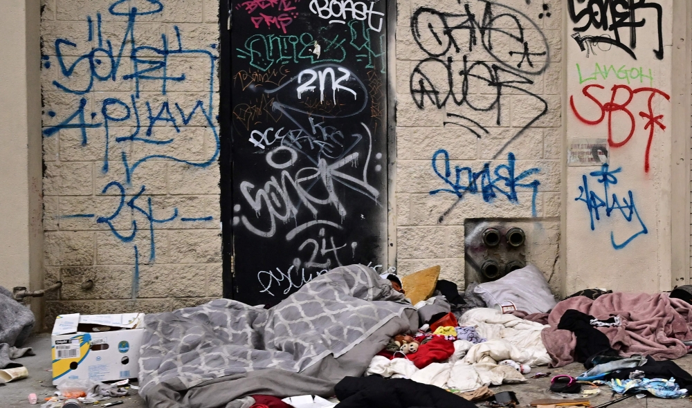 A homeless person sleeps beneath a blanket on a sidewalk in Skid Row in Los Angeles, California, on April 22, 2024. The US Supreme Court is considering the issue of homelessness and whether cities can ban people from sleeping outdoors when space for shelter is lacking. (Photo by Frederic J. BROWN / AFP)
