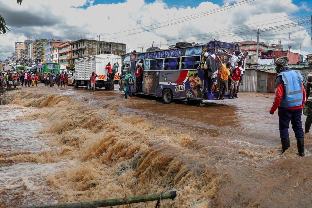 Pedestrians hang off the back of a matatu (public transport bus) to avoid having to wade across a flooded section of road after a stream burst it's banks overnight following heavy seasonal rain in the capital, Nairobi on April 24, 2024. (Photo by Tony KARUMBA / AFP)

