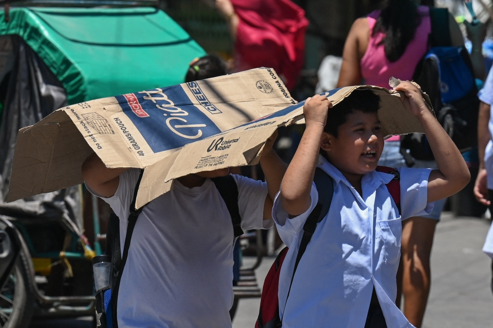 Students use a cardboard to protect themselves from the sun during a hot day in Manila on April 2, 2024. (Photo by Jam Sta Rosa / AFP)

