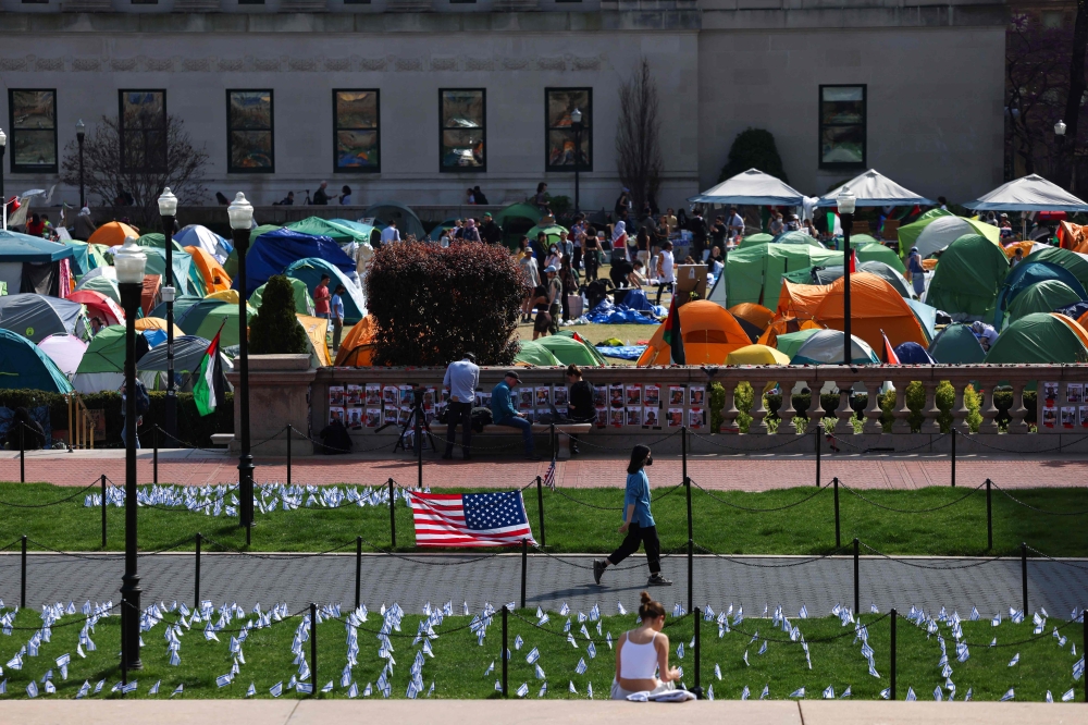 A woman walks past Israeli and US flags alongside portraits of Israelis taken hostage by the militant Palestinian group Hamas in front of the pro-Palestinian encampment at the Columbia University on April 28, 2024 in New York City. Photo by Charly TRIBALLEAU / AFP. 