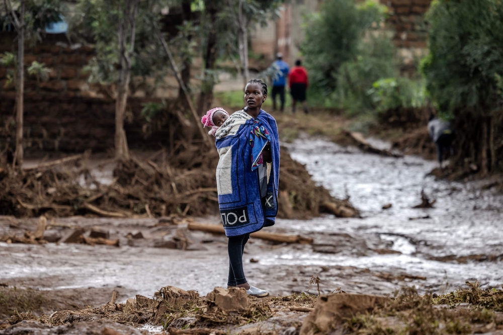 A woman carrying her baby on the back looks on near her house in a muddy area heavily affected by torrential rains and flash floods in Mai Mahiu, on April 29, 2024. Photo by LUIS TATO / AFP