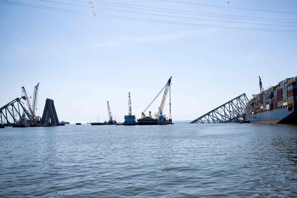 The cargo ship Dali (R) remains stuck in the wreckage of the Key Bridge as workers remove debris from the Patapsco River entrance to Baltimore Harbor on May 2, 2024, in Baltimore, Maryland. Photo by Brendan Smialowski / AFP