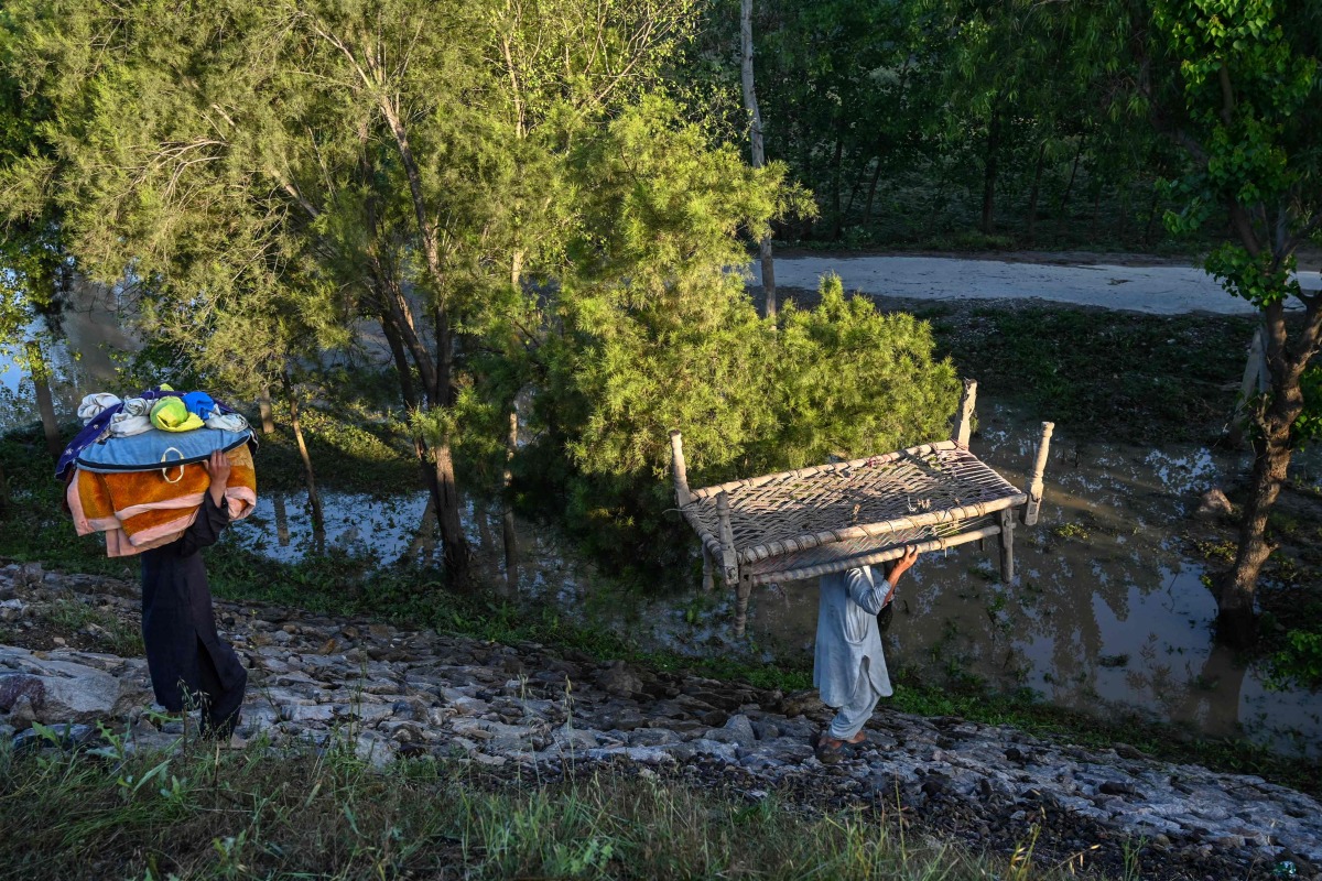 A displaced family carry their belongings to tents at a makeshift camp after fleeing from their flood hit homes following heavy rains in Charsadda district of Khyber Pakhtunkhwa province on April 17, 2024. (Photo by Abdul Majeed/ AFP)


