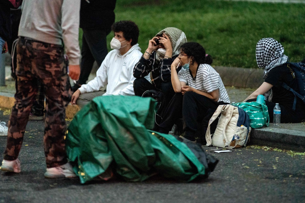 People from a Pro-Palestinian encampment sit on the sidewalk along I St NW after Law Enforcement cleared George Washington University's University Yard at on May 8, 2024 in Washington, DC. (Photo by Kent Nishimura / GETTY IMAGES NORTH AMERICA / Getty Images via AFP)