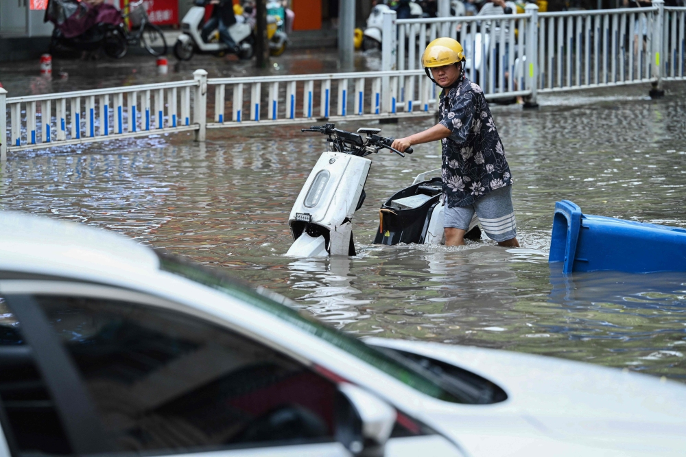 This photo taken on May 19, 2024 shows a man pushing his scooter along a flooded street following heavy rains in Nanning, in China's southern Guangxi region. (Photo by AFP)