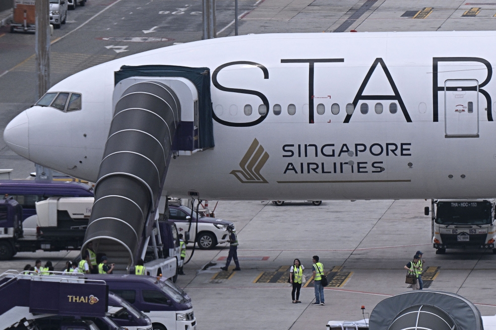 Officials gather around the Singapore Airlines Boeing 777-300ER airplane as it is parked on the tarmac at Suvarnabhumi International Airport in Bangkok on May 22, 2024. (Photo by Lillian Suwanrumpha / AFP)