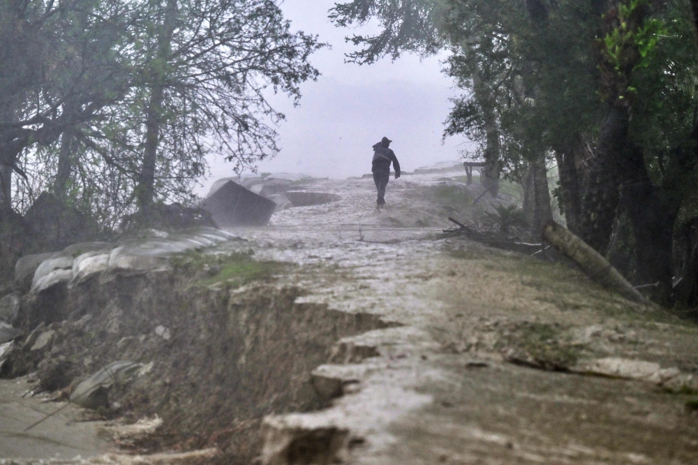 A man walks on a damaged embankment along the Sonatola river during heavy rainfall in Patuakhali on May 27, 2024, following the landfall of Cyclone Remal in Bangladesh. Photo by Munir Uz Zaman / AFP.