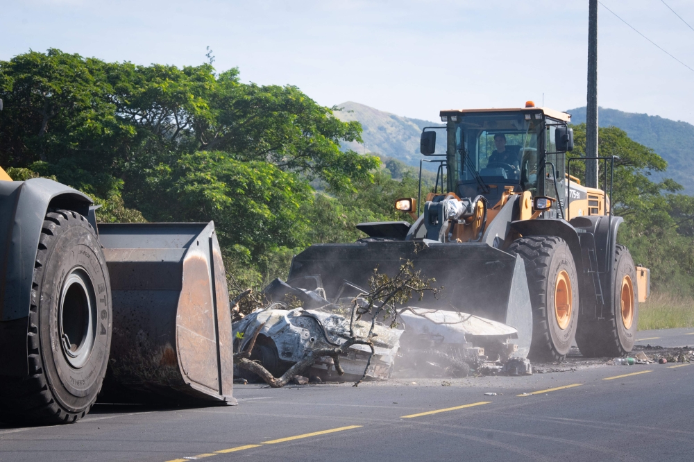 A tractor clears branches and a smashed car from a roadblock on the RT1 near the Ondemia district in Paita in France's Pacific territory of New Caledonia, June 4, 2024. (Photo by Delphine Mayeur / AFP)