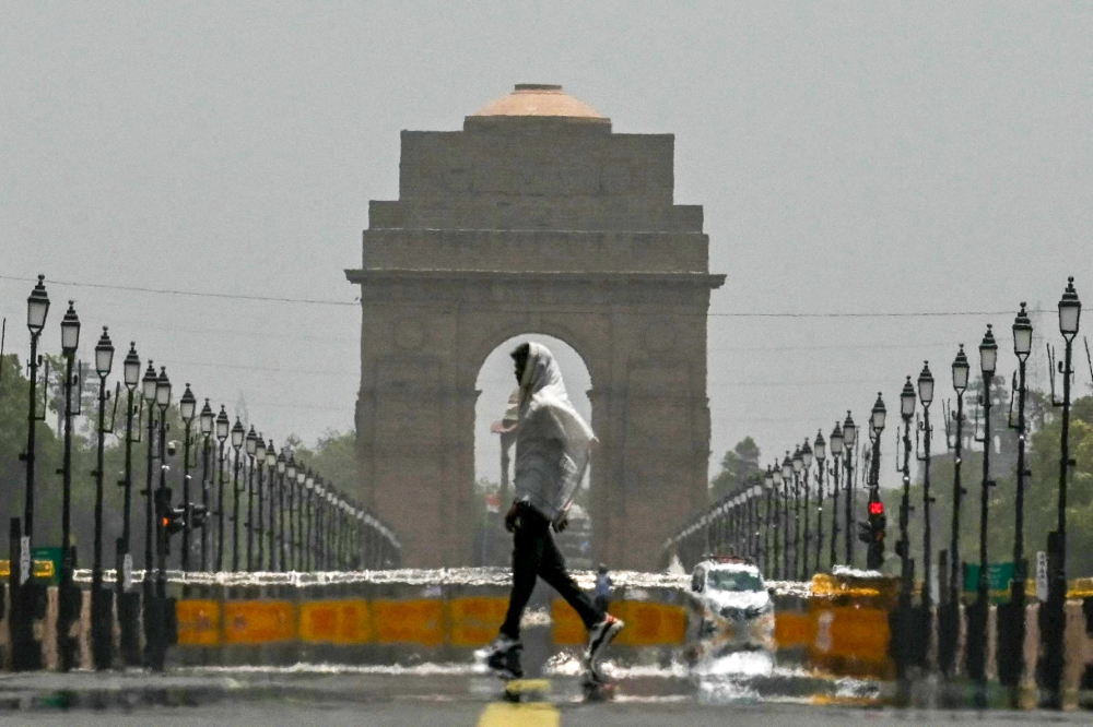 A man wears a scarf as he walks past the India Gate on a hot summer day in New Delhi on June 18, 2024. (Photo by Arun Sankar / AFP)