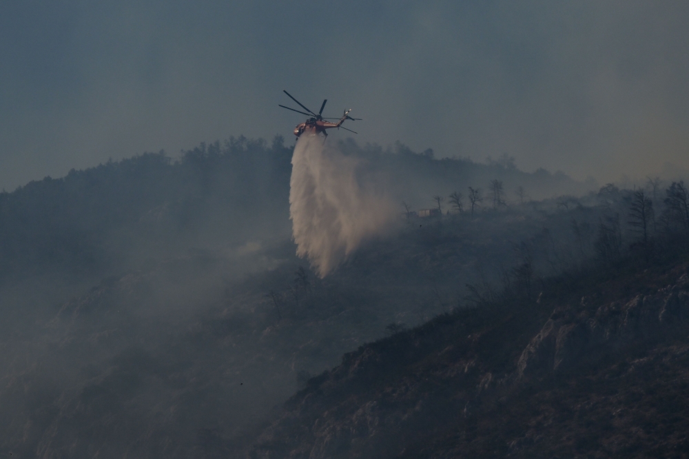 A helicopter sprays water above a wild fire at mount Parnitha, in Parnitha near Athens, on June 29, 2024. (Photo by Aris Messinis / AFP)