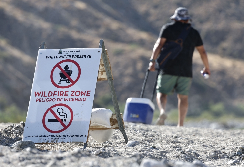 A person walks past a 'Wildfire Zone' sign on their way to cool off in the Whitewater River on July 2, 2024 in Whitewater, California. (Photo by Mario Tama/Getty Images/AFP)

