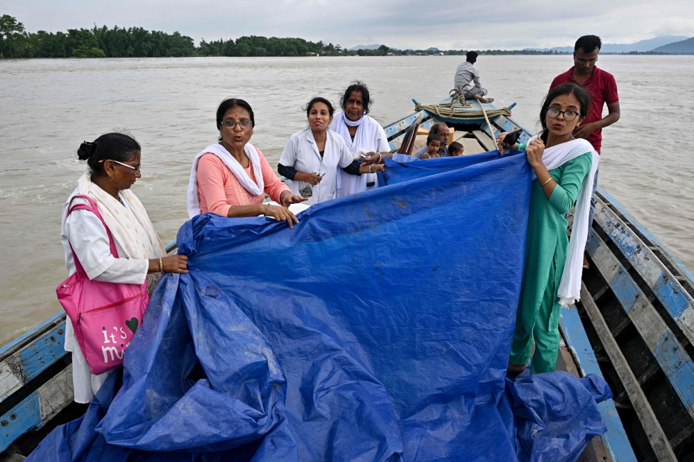 Members of a medical team hold a tarpaulin as a woman delivers a child on a boat on July 3, 2024. (Photo by Biju Boro / AFP)
 
