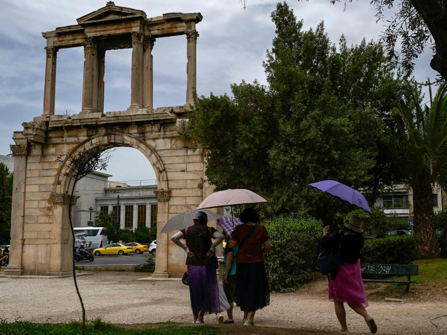 (Files) Tourists holding umbrellas walk in front of the ancient Roman Andrian Gate, during a hot day in Athens on June 13, 2024. (Photo by Aris Messinis / AFP)