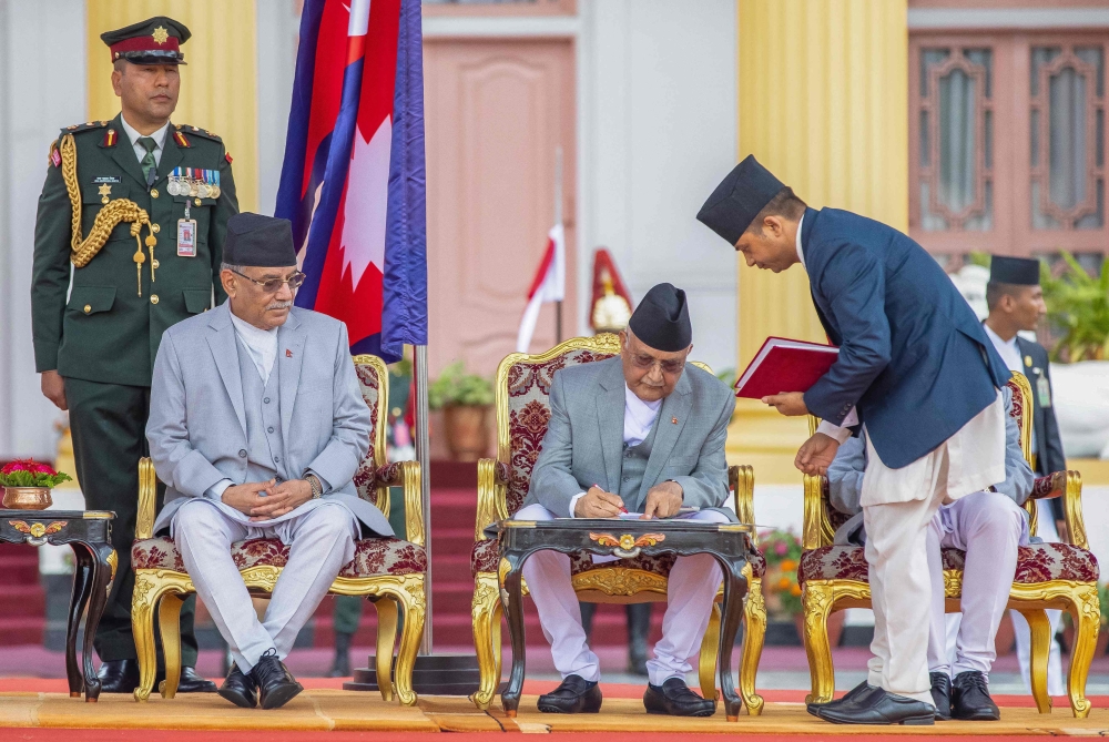 Nepal's newly appointed prime minister Khadga Prasad Sharma Oli (C) signs a document as his predecessor Pushpa Kamal Dahal looks on at the presidential house in Kathmandu on July 15, 2024. (Photo by Prabin Ranabhat / AFP)