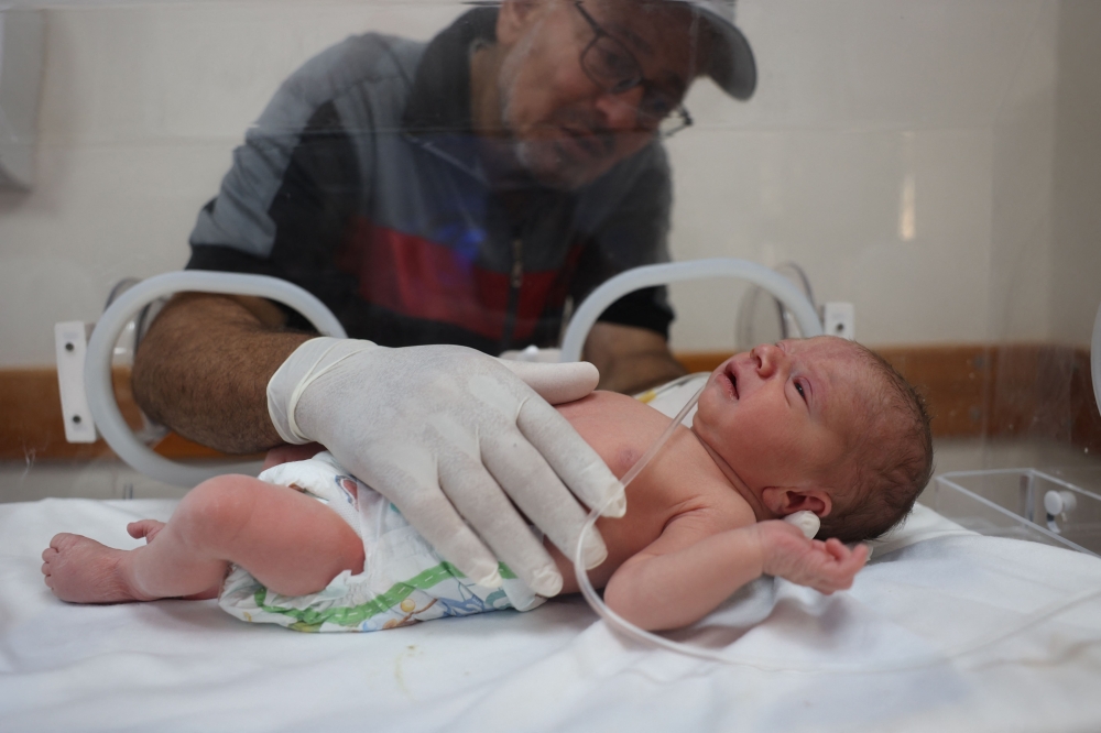 The newborn being caressed by his grandfather as he lies in an incubator at the al-Awda hospital in Deir el-Balah on July 20, 2024. (Photo by Eyad Baba / AFP)