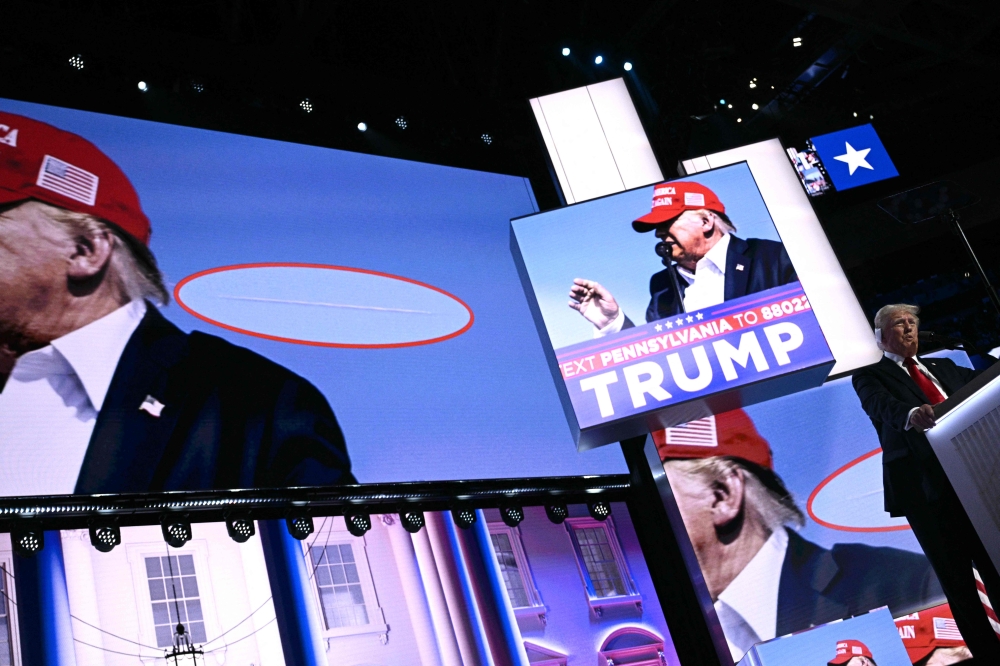 A photo showing a bullet going past US former President and 2024 Republican presidential candidate Donald Trump's head during an assassination attempt is shown on screen as he speaks onstage during the last day of the 2024 Republican National Convention at the Fiserv Forum in Milwaukee, Wisconsin, on July 18, 2024. (Photo by Brendan SMIALOWSKI / AFP)
