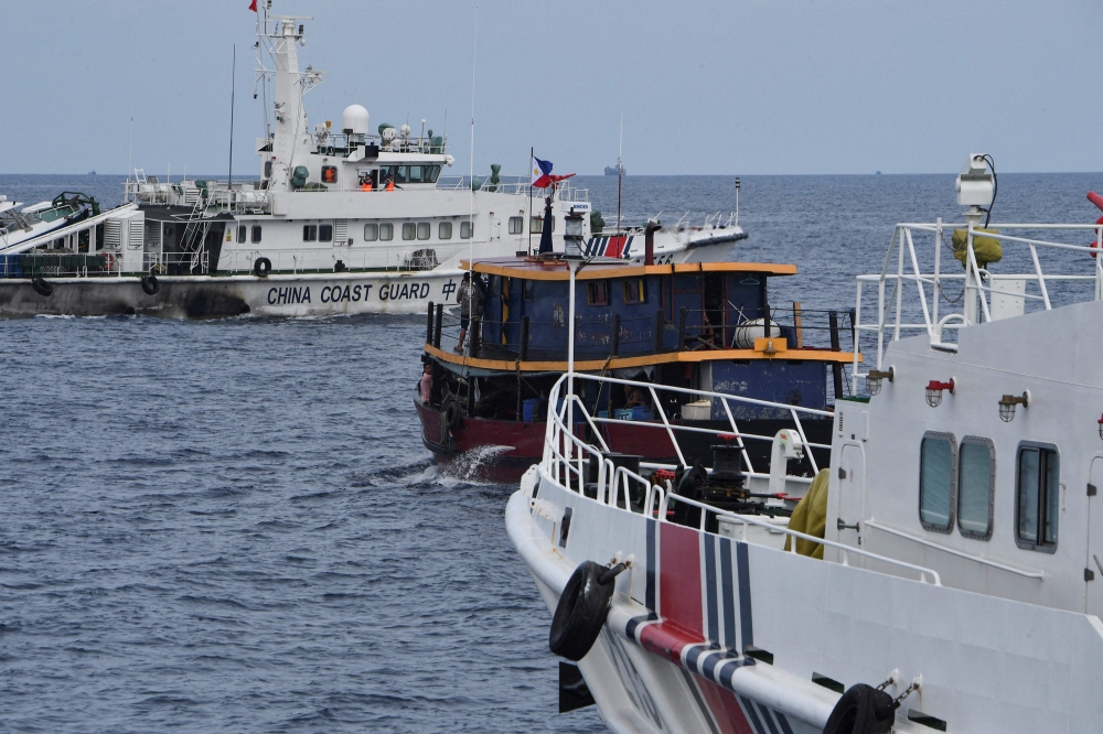 This file photo taken on August 22, 2023 shows Chinese coast guard ships (L and R) corralling a Philippine civilian boat chartered by the Philippine navy to deliver supplies to the Philippine navy ship BRP Sierra Madre, in disputed waters of the South China Sea. Photo by Ted ALJIBE / AFP