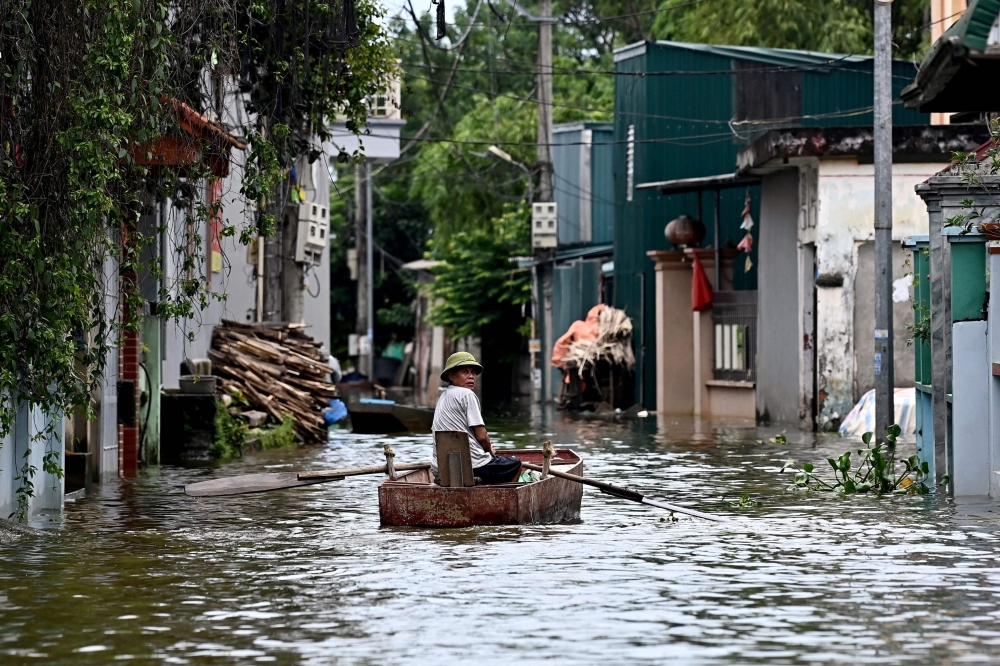 This photo taken on July 28, 2024 shows a man rowing a boat through flood waters in Ben Voi village on the outskirts of Hanoi. Photo by Nhac NGUYEN / AFP