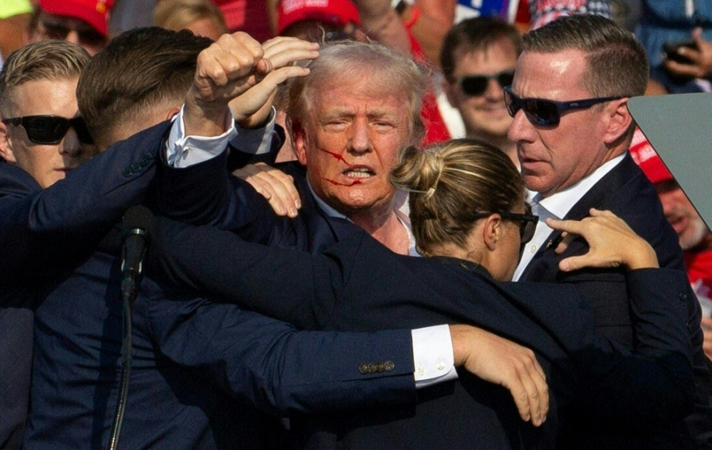 (Files) Republican candidate Donald Trump is seen with blood on his face surrounded by secret service agents as he is taken off the stage. (Photo by Rebecca Droke / AFP)

