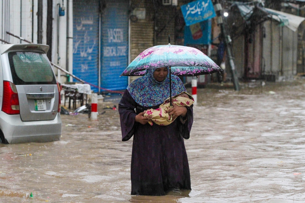 A woman carries her infant as she wades through a flooded street during heavy rainfall in Lahore on August 1, 2024. (Photo by Syed Murtaza / AFP)

