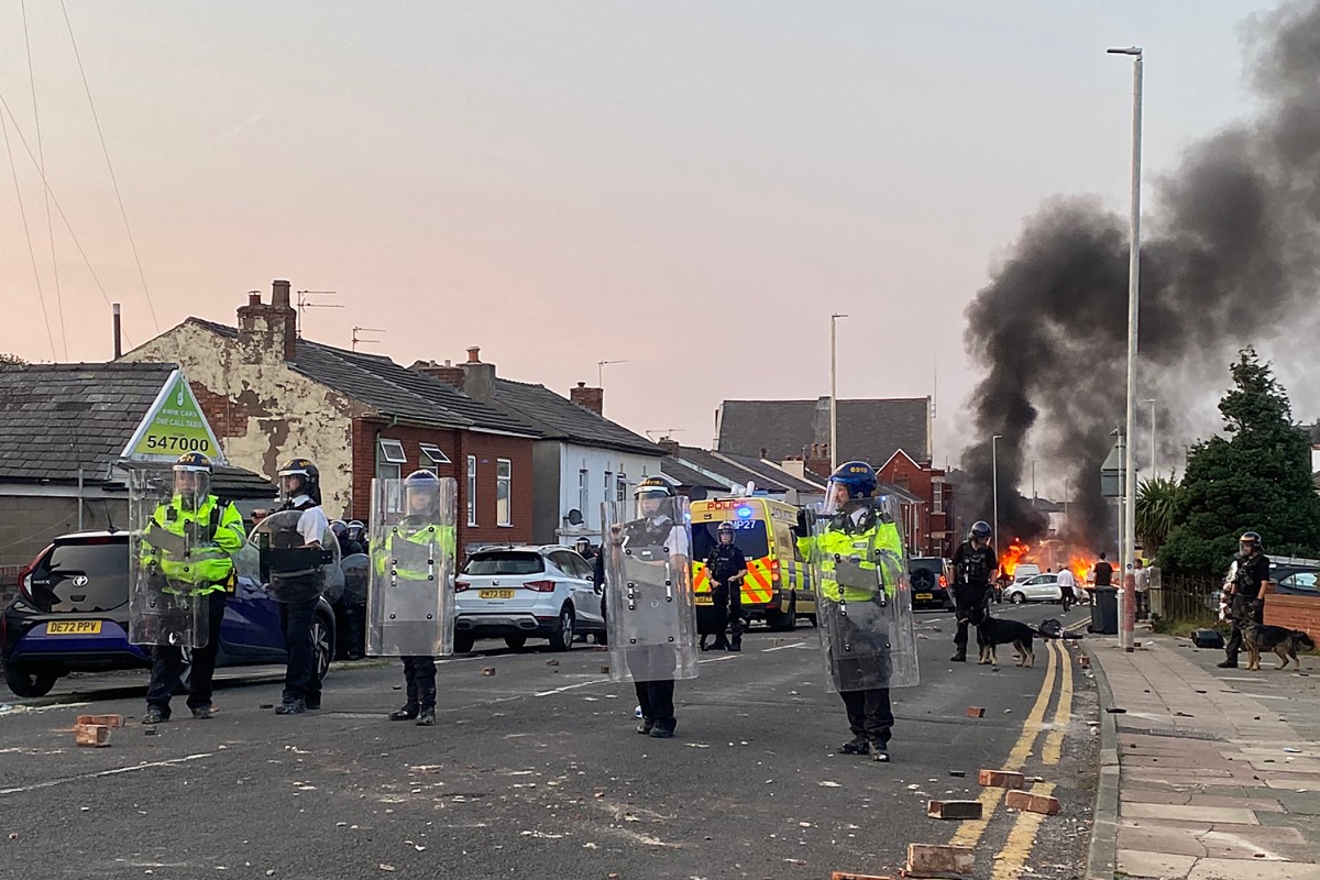 Smoke billows from a fire started by protesters as riot police stand guard after disturbances in Southport, northwest England, on July 30, 2024, a day after a deadly child knife attack. Photo by Roland LLOYD PARRY / AFP
