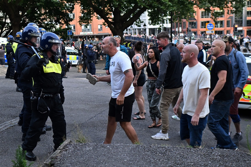 A protester holding a piece of concrete walks towards riot police as clashes erupt in Bristol on August 3, 2024 during the 'Enough is Enough' demonstration held in reaction to the fatal stabbings in Southport on July 29. (Photo by JUSTIN TALLIS / AFP)
