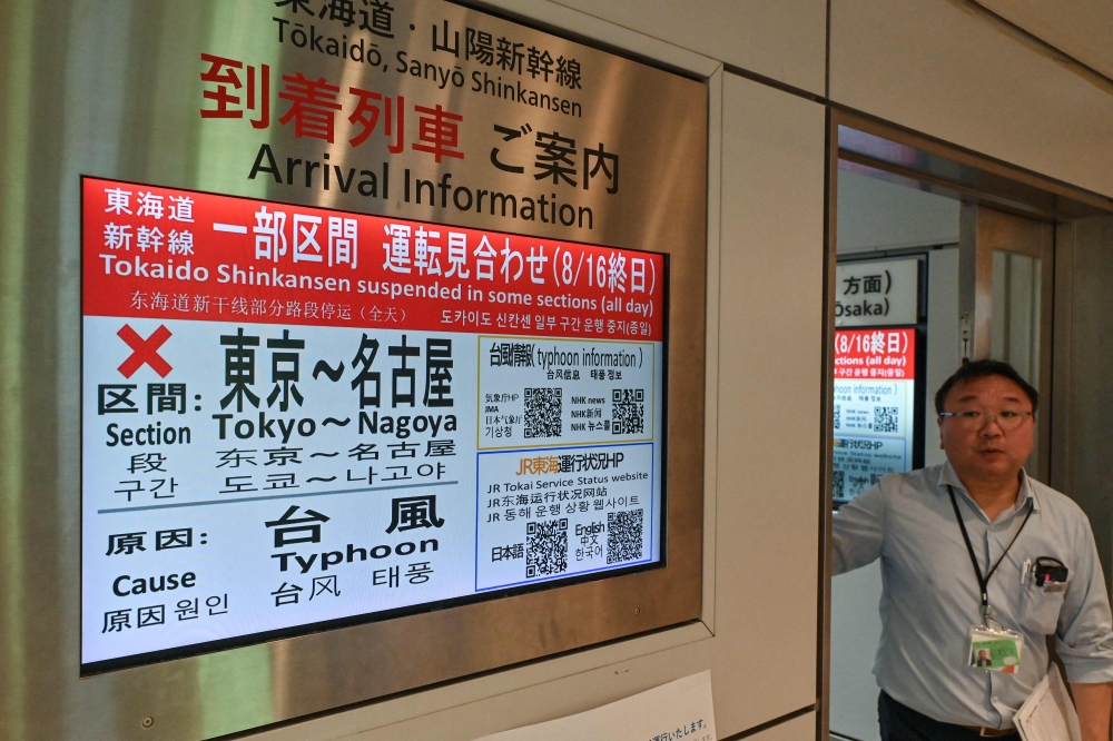 A train station employee walks out of an office next to a digital display informing passengers that the high-speed bullet train, or 