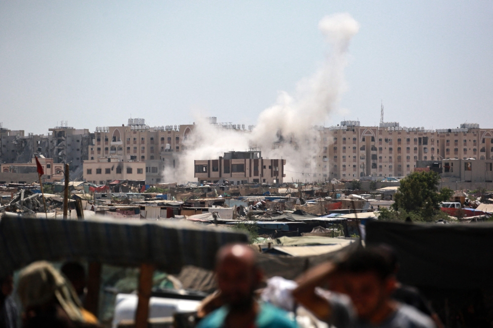 Displaced Palestinians watch from a makeshift camp as shells fired from Israeli tanks hit an area near the Hamad residential complex in Khan Yunis in the southern Gaza Strip on August 18, 2024, amid the ongoing conflict between Israel and the Hamas militant group. (Photo by Bashar TALEB / AFP)
