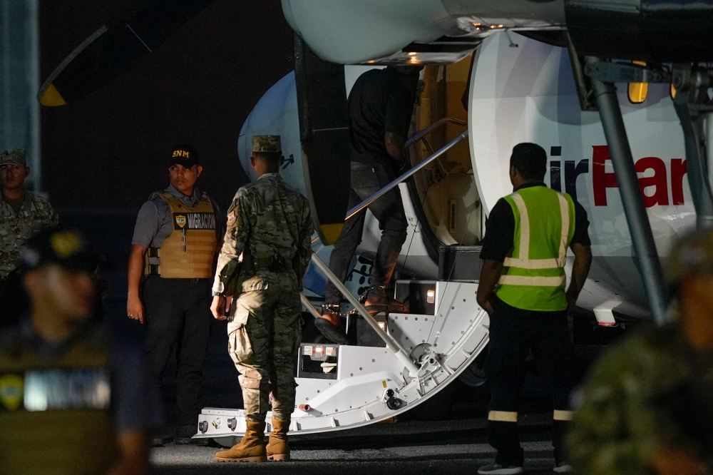 A Colombian migrant, with his hands and feet handcuffed, climbs a plane at the Albrook Gelabert airport in Panama City on August 20, 2024, during his deportation. (Photo by ARNULFO FRANCO / AFP)
