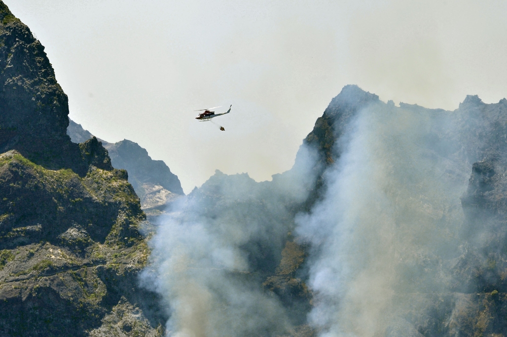 A Regional Civil Protection Service helicopter fights a wildfire raging through Pico do Areeiro mountain on August 21, 2024 in Santana on the Portuguese island of Madeira, which broke out one week ago in the Ribeira Brava district. (Photo by Helder Santos / AFP)
