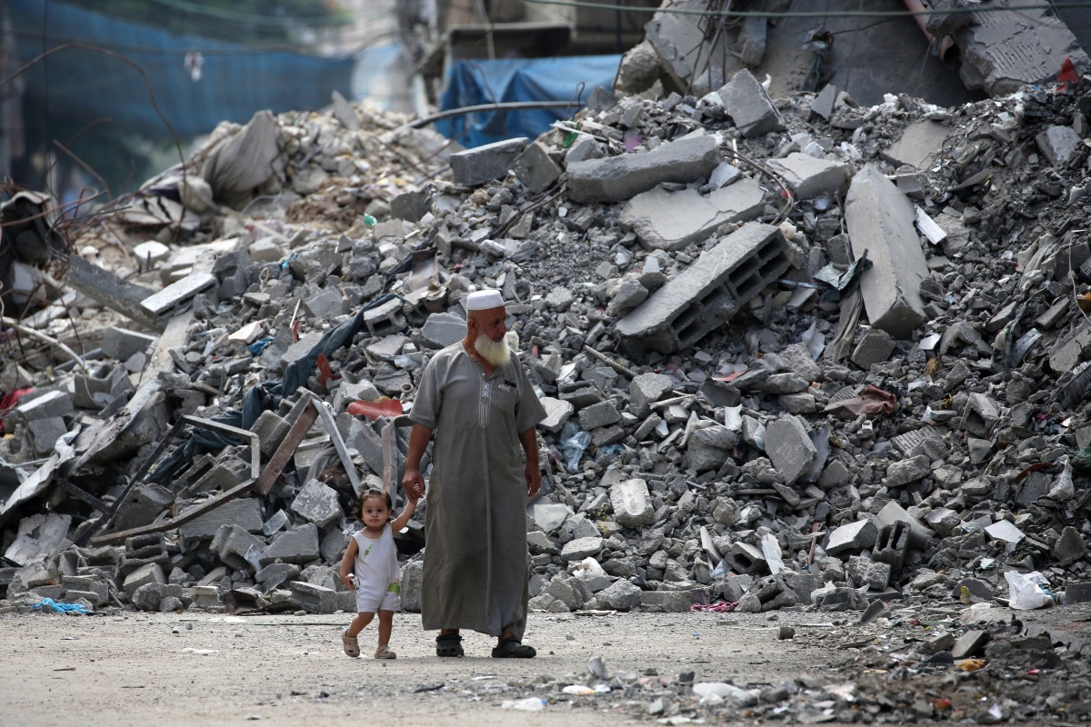 An elderly man holds a child by the hand as he walks past a building levelled by Israeli bombardment in the Bureij refugee camp in central Gaza Strip on August 25, 2024, amid the ongoing conflict between Israel and the Palestinian Hamas militant group. (Photo by Eyad BABA / AFP) 