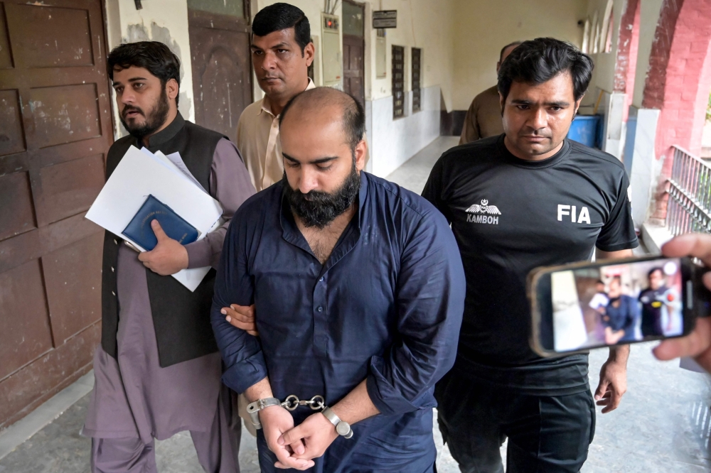 Farhan Asif (2R), who was arrested allegedly over cyber terrorism, is escorted by Pakistan's Federal Investigation Agency (FIA) personnel after his acquittal from a court in Lahore on August 26, 2024. (Photo by Arif ALI / AFP)
