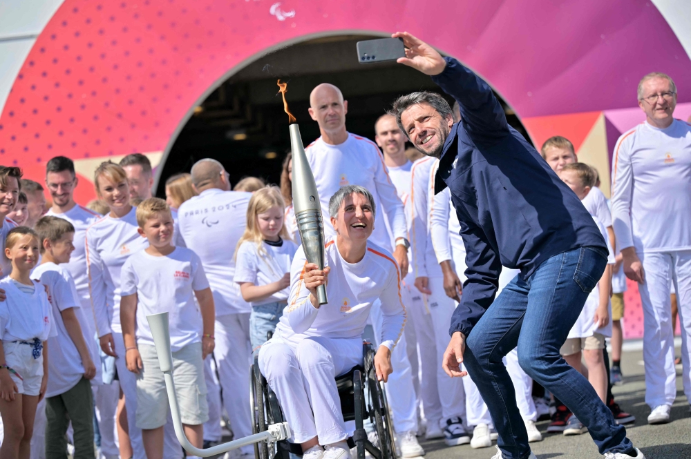 French President of the Paris 2024 Olympics and Paralympics Organising Committee (COJO) Tony Estanguet (right) takes a selfie with former French wheelchair fencer Emmanuelle Assmann holding the torch of the Paris 2024 Paralympic Games after arrival of the Paralympics flame at the entrance of the Channel Tunnel in Coquelles, northern France on August 25, 2024. (Photo by Lou Benoist / AFP)