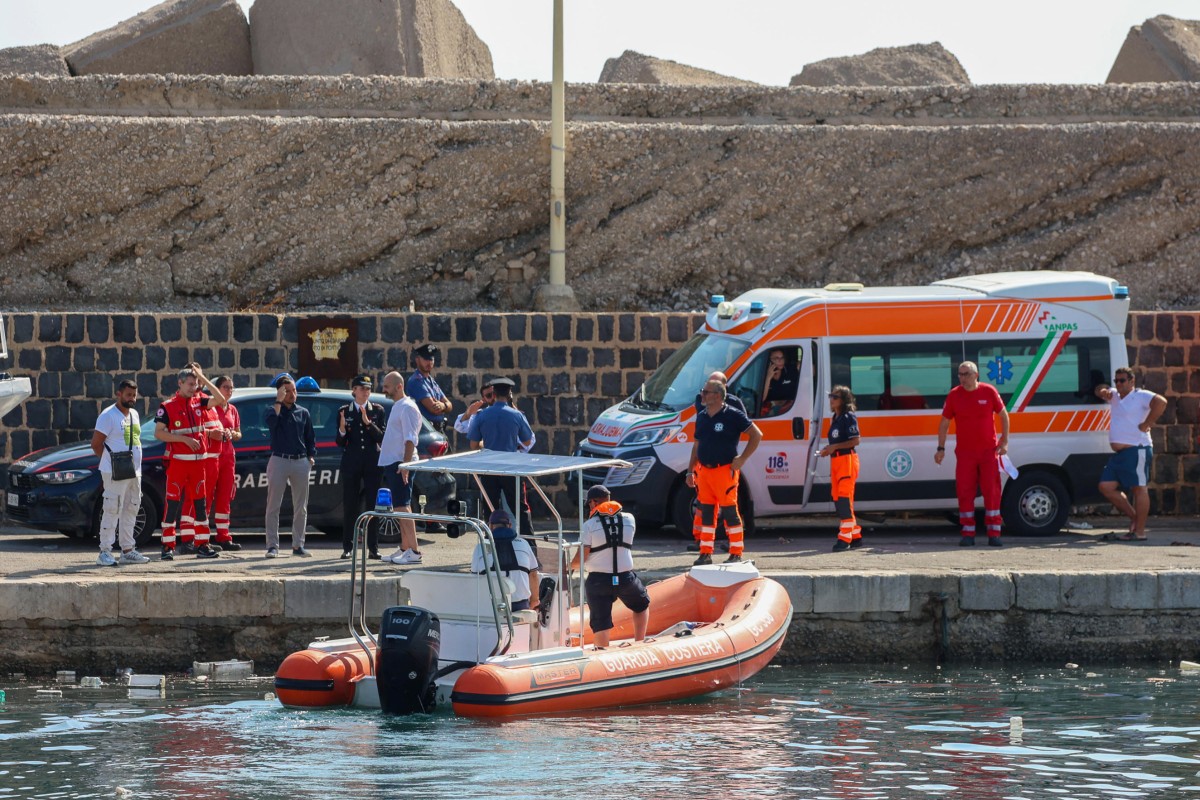 Italian Carabinieri stand on the quay with health workers look at a Coast Guard boat prepares to search for six others missing after recovering a victim due to a sailboat sank off the coast of Porticello, nosthwestern of Sicily Island, on August 19, 2024. (Photo by Igor Petyx / ANSA / AFP)

