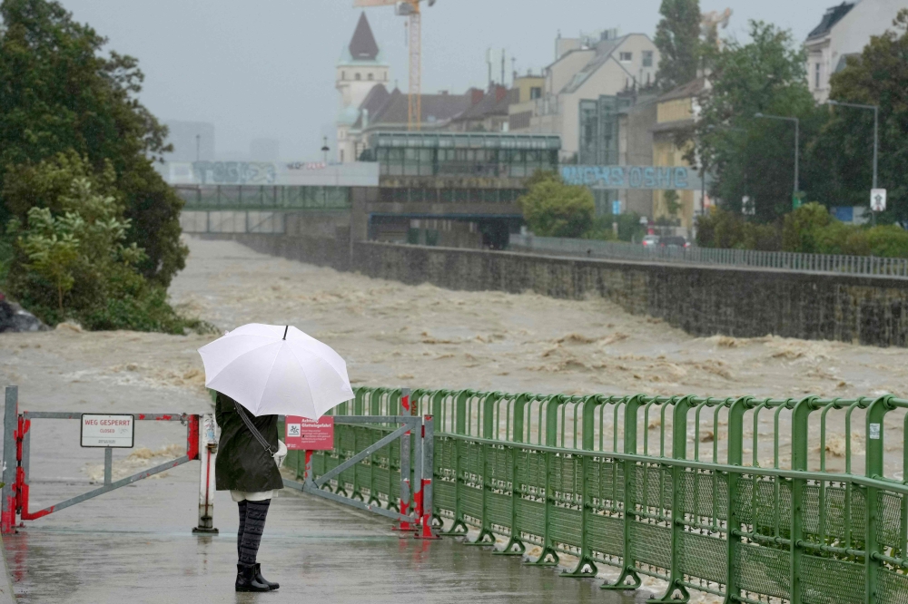 A pedestrian looks at the high level of the Wien river in Hutteldorf, Vienna, during heavy rainfall on September 15, 2024. (Photo by Georg Hochmuth / APA / AFP)