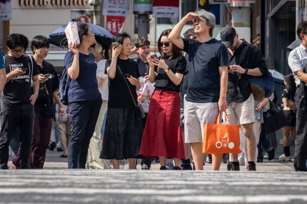 People wait to cross a street during hot weather in Tokyo on September 19, 2024. (Photo by Yuichi Yamazaki / AFP)
