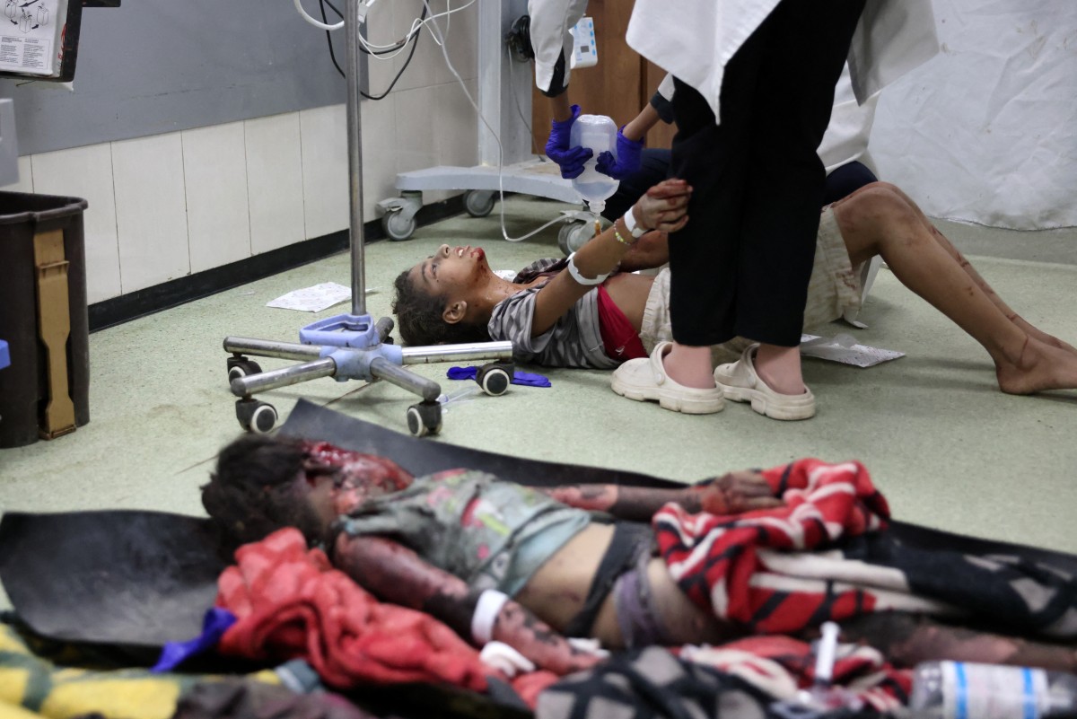 Graphic content / A dead child lies on the ground as a young Palestinian girl receives medical care for her injuries sustained in an Israeli strike near Khan Yunis in the southern Gaza Strip, at the Nasser hospital on September 18, 2024. Photo by Bashar TALEB / AFP.