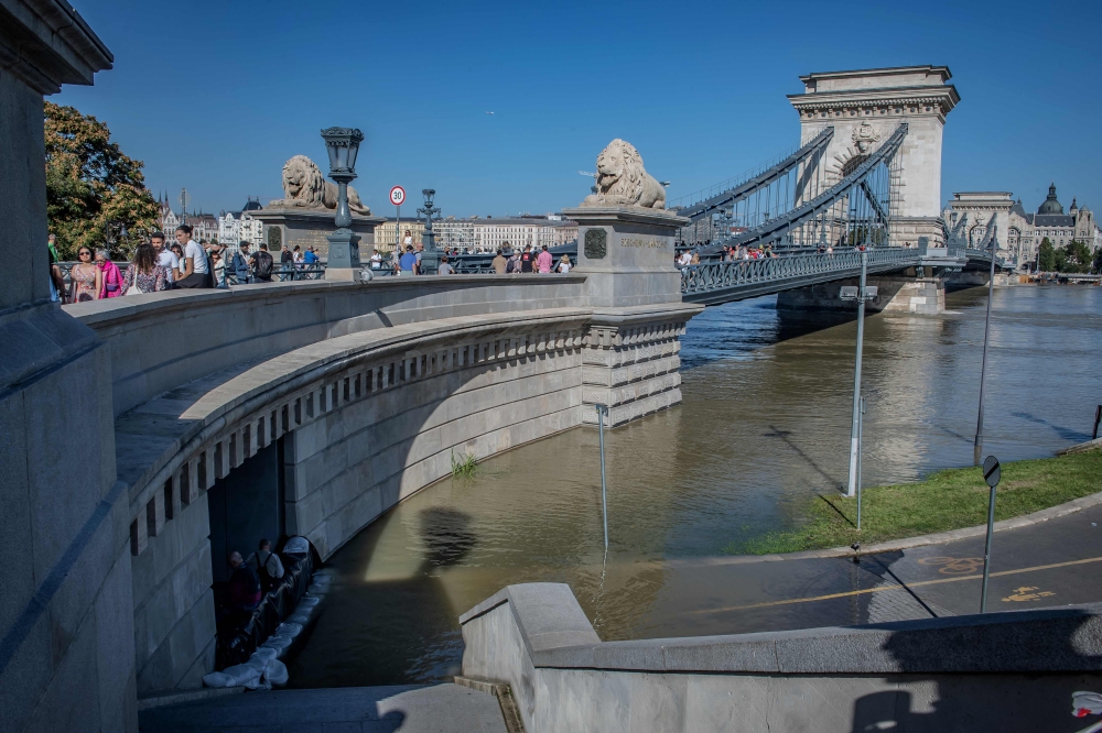 Pedestrians walk across The Szechenyi Chain Bridge as workers help to protect a tunnel with sandbags, near Buda Castle on September 21, 2024. (Photo by FERENC ISZA / AFP)