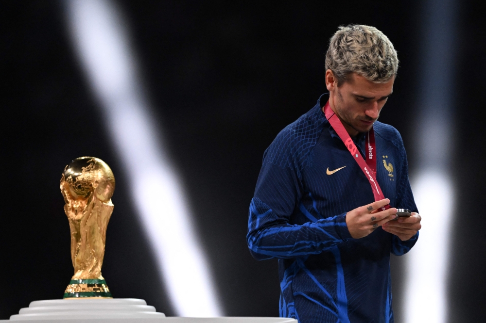 France's forward #07 Antoine Griezmann looks at his silver medal as he walks past the FIFA World Cup trophy during the trophy ceremony after France lost the Qatar 2022 World Cup final football match between Argentina and France at Lusail Stadium in Lusail, north of Doha on December 18, 2022. Photo by Kirill KUDRYAVTSEV / AFP