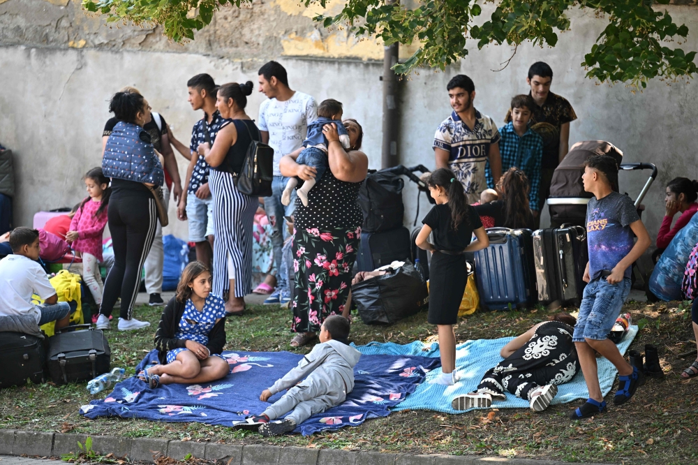 Refugees sit on the pavement close to their former shelter in Kocs village, about 70 km north-west from the Hungarian capital Budapest, on August 21, 2024. (Photo by Attila Kisbenedek / AFP)