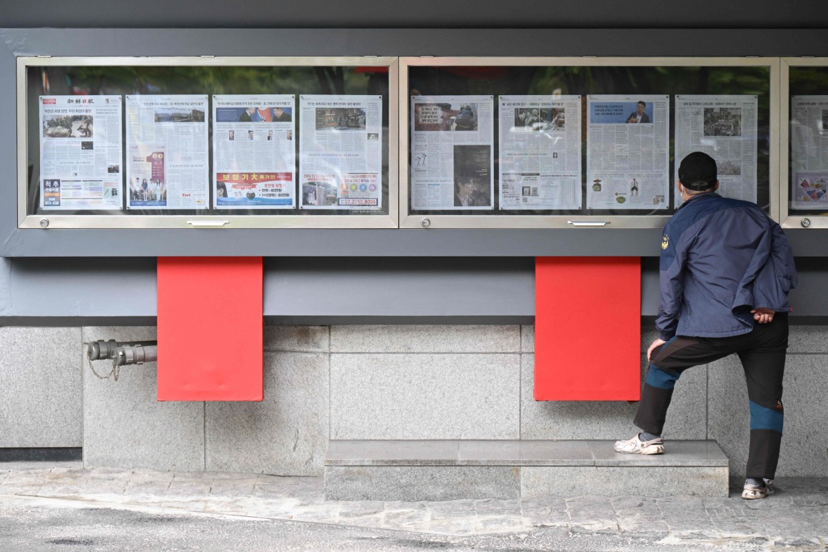 A man reads a newspaper displayed on a street for the public in Seoul on October 21, 2024, with coverage (in left case) on North Korea's decision to deploy thousands of soldiers to Ukraine's front lines. (Photo by Anthony WALLACE / AFP)
