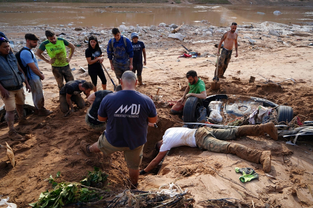 A group of people try to dig up a car in search of victims buried on the riverbank, on November 1, 2024, after a flooding devastated the town of Paiporta, in the region of Valencia, eastern Spain. (Photo by Manaure Quintero / AFP)