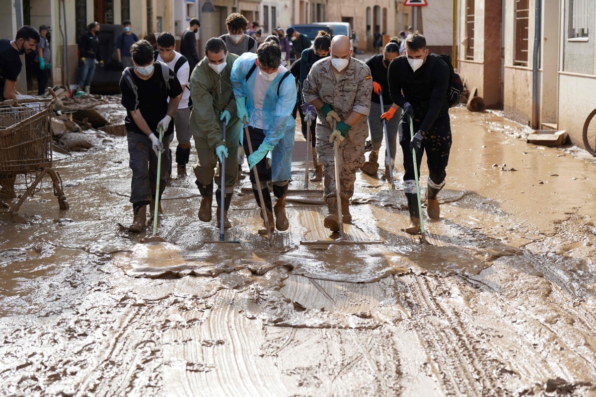 People with masks and soldier remove mud in a flooded street on November 6, 2024, in Catarroja, in the region of Valencia, eastern Spain, in the aftermath of deadly floods. (Photo by CESAR MANSO / AFP)
