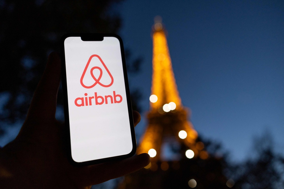 This photograph taken on October 28, 2024 shows the logo of short-term housing rentals online application Airbnb on a smart-phone screen in front of the Eiffel Tower in Paris. Photo by Grégoire CAMPIONE / AFP